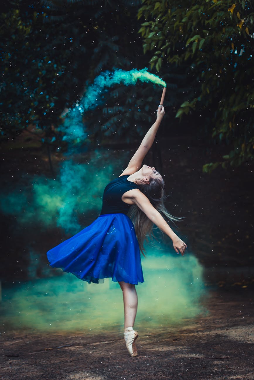 woman standing by one foot and holding flare stick near trees