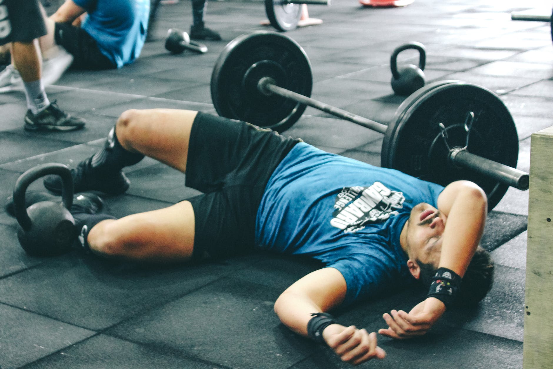 man lying on rubber mat near barbell inside the gym